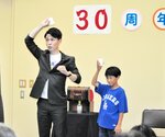 紙コップの水を消す技に挑戦する片山さん（左）＝新温泉町浜坂の加藤文太郎記念図書館