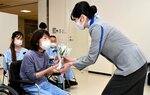 ＡＮＡ客室乗務員の山田さん（右）からスズランを受け取る入院患者ら＝２３日、鳥取市の鳥取赤十字病院
