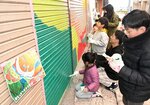 シャッターにペンキを塗る参加者。左は完成図＝２４日、ＪＲ鳥取駅前のサンロード商店街