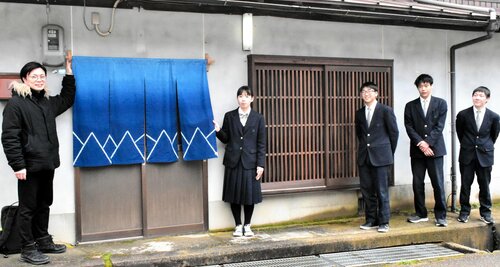 藍染めののれんと格子戸の前で笑顔を見せる生徒と星野さん（左）