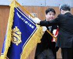 中田教育長から新しい校旗を受け取る井上校長（左）