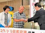 関貫市長（右）らから記念品などを受け取る榎並光治さん、万里子さん夫妻＝２６日、豊岡市岩井のコウノトリ但馬空港