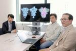 　生成ＡＩが予測したタンパク質の形態変化について、画像を示し説明する京大教授の奥野恭史さん（左）ら＝５月、東京都内