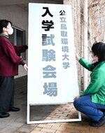 会場玄関前に大きな看板を設置する職員ら＝２１日、鳥取市若葉台北１丁目の鳥取環境大