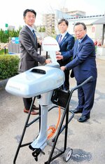 引き渡された電動船外機を前に福田部長（左）から鍵を受け取る上定市長（中央）と能海理事長