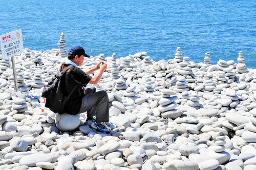 ゴール記念　鳴り石の浜にゴール後、高く積まれた石をスマホで撮影するウオーカー＝３日、琴浦町赤碕