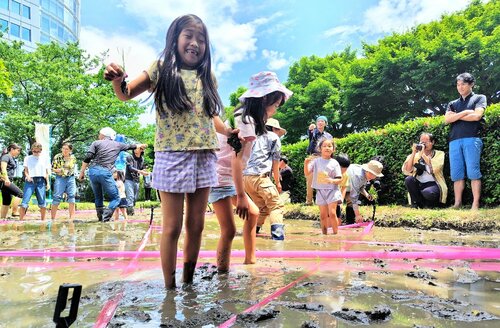 苗を手に、泥の感触に笑顔を見せる子ども