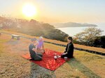 米子城跡からの夕日を背に茶会を開く山田さん（右）＝２日、米子市久米町