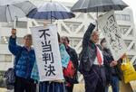 　伊方原発３号機の運転差し止めが認められず、松山地裁前で「不当判決」などと書かれた垂れ幕を掲げる原告ら＝１８日午後