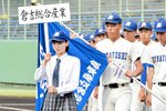 入場行進でプラカードを掲げてチームを先導する倉吉総産マネジャーの福井さん（左）＝ヤマタスポーツパーク野球場