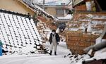 　雪が積もる石川県輪島市で、倒壊した家屋の前を歩く男性＝１６日午前