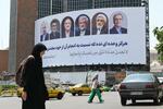 　１５日、イランの首都テヘランで全身を覆う黒い衣装を着た女性。後ろには大統領選候補者の看板が設置されていた（共同）