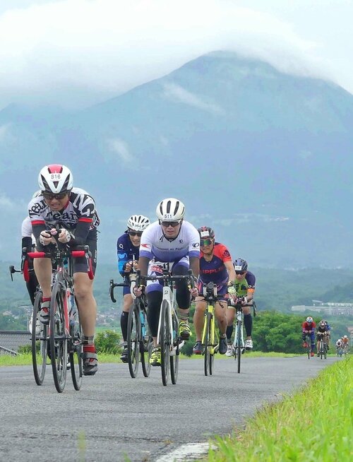 雲にかすむ大山をバックにバイクで力走する出場者＝１４日、鳥取県米子市東八幡