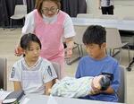 　「子ども大学くまもと」で、赤ちゃんの人形を抱く参加者＝８月、熊本市