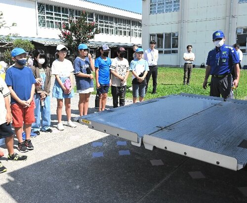 重い荷物を持ち上げるトラックの機能の説明を聞く児童ら