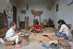　ネパールの首都カトマンズ近郊のブンガマティで、長男（左）を工房で遊ばせながら黙々と伝統楽器を彫るパルミラ・タマンさん（中央）＝２０２４年６月（共同）