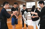 剣道部員に教えてもらいながら、木刀で新聞を切る練習をする留学生ら＝２５日、鳥取市西品治の鳥取城北高