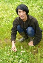 　山梨県北杜市にある自宅の庭に咲いたシロツメクサの花と触れ合う鈴木純さん