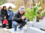 みぞれまじりの雨が降る中、墓石に手を合わせる家族連れ＝２０日、鳥取市八坂のいなば墓苑