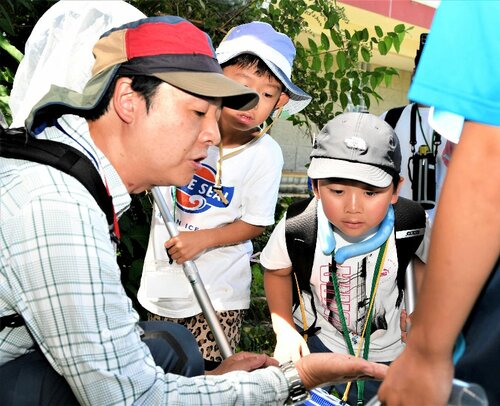 虫網でつかまえた数ミリほどの昆虫を子どもたちに見せる鶴さん（左）＝７日、若桜町つく米の氷ノ山自然ふれあい館響の森