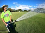 暑さの中、芝生に水をまくボランティアスタッフ＝１０日、米子市皆生温泉３丁目の皆生プレイパーク