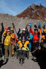 　富士山頂に到達し、山岳用車いすに乗りながら万歳する９０歳の冒険家三浦雄一郎さん（中央）。後ろは次男の豪太さん＝３１日朝