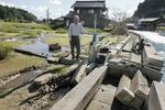 　壊れた護岸の脇に立つ泊一夫さん。海水が侵入し水田だった場所は沼と化した。奥は近隣住民の家＝１３日、石川県穴水町