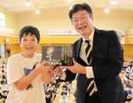 森本局長（右）から「決定版　ゲゲゲの鬼太郎」の全１４巻を受け取る島谷さん＝３日、境港市湊町の境小