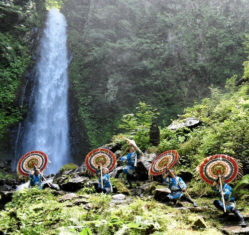 ごうごうと流れ落ちる滝の前でポーズを取る傘踊り保存会のメンバーら＝３日、鳥取市国府町雨滝