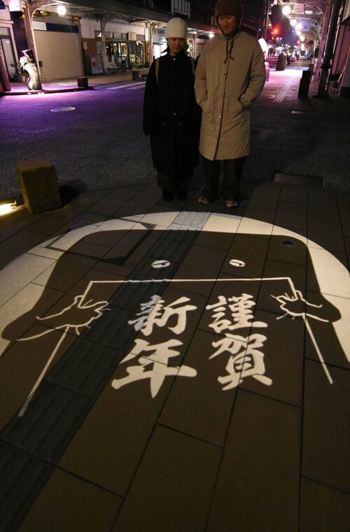 歩道に浮かび上がる正月にちなんだ図柄の妖怪影絵＝昨年１２月２６日夜、境港市松ケ枝町