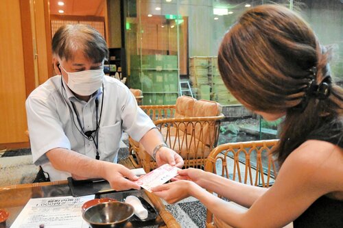 宿泊客（右）にクーポン券を手渡す旅館スタッフ＝６日、三朝町山田の万翠楼