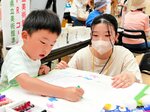 クレヨンで絵を描き、てるてるぼうずを作るワークショップで子どもを見守る油谷さん＝２４日、倉吉未来中心