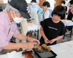 蓄養ウニと天然サザエの網焼きに挑戦する参加者＝１７日、鳥取市賀露町西４丁目の賀露港