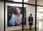 　透明な板の向こうに展示されている肖像写真。「ポートレイト・プロジェクト」の作品は連日、展示替えする。右は担当した川島拓人さん