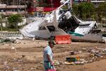　２８日、メキシコ南部ゲレロ州アカプルコで、損傷したボートの近くを歩く男性（ロイター＝共同）