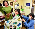 ６年間伸ばした髪を切り、手にする香織さん（左）と髪を切る寛菜さん（中央）＝倉吉市新町２丁目の女神美容室