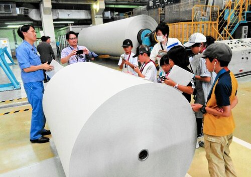 製造された新聞巻き取り用紙を前に、説明を聞く児童ら＝２７日、愛媛県四国中央市の大王製紙三島工場